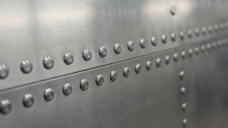 Detalle de remaches macizos instalados en panel de fuselaje aeronáutico, mostrando la precisión requerida en aplicaciones estructurales